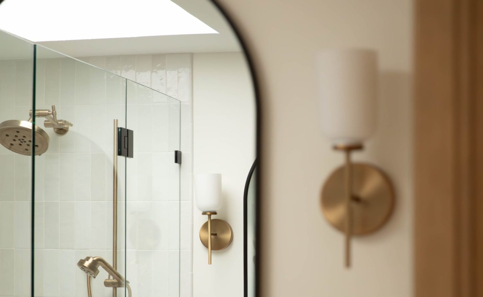 Arch mirror with gold sconces above a bathroom vanity installed by Sylvania bathroom remodeler